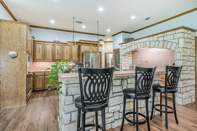 7 Pebble Beach Ct, Amarillo, TX 79124 - kitchen featuring appliances with stainless steel finishes, tile countertops, ornamental molding, backsplash, and a breakfast bar