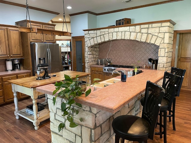 7 Pebble Beach Ct, Amarillo, TX 79124 - kitchen with stainless steel fridge, tile countertops, a breakfast bar area, brown cabinets, and ornamental molding