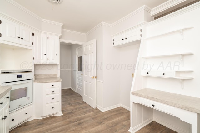 kitchen featuring dark hardwood / wood-style flooring, crown molding, oven, and white cabinets