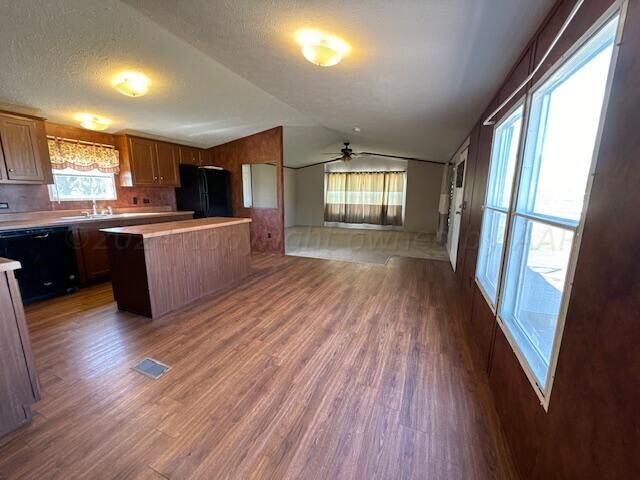 kitchen with black appliances, ceiling fan, lofted ceiling, a center island, and dark wood-type flooring