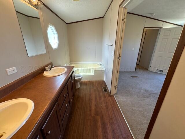 bathroom with a textured ceiling, wood-type flooring, vanity, a washtub, and toilet