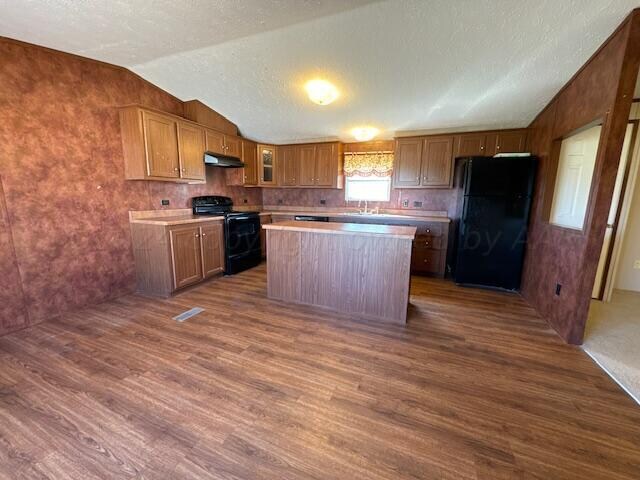 kitchen with black appliances, a kitchen island, a textured ceiling, vaulted ceiling, and dark wood-type flooring