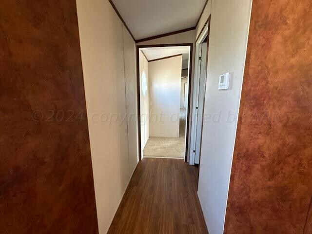 corridor featuring ornamental molding, dark hardwood / wood-style flooring, and vaulted ceiling