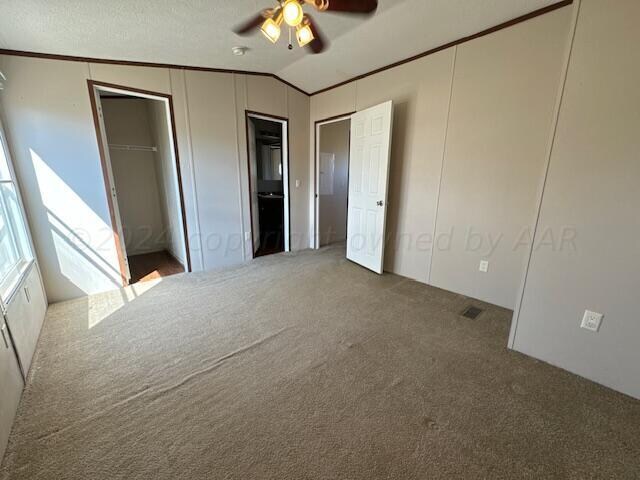 unfurnished bedroom featuring lofted ceiling, a textured ceiling, carpet, and ceiling fan