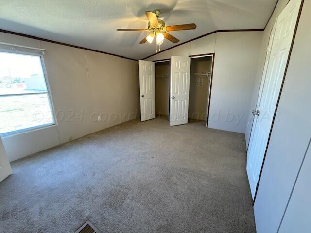 unfurnished bedroom with lofted ceiling, ceiling fan, two closets, and light carpet