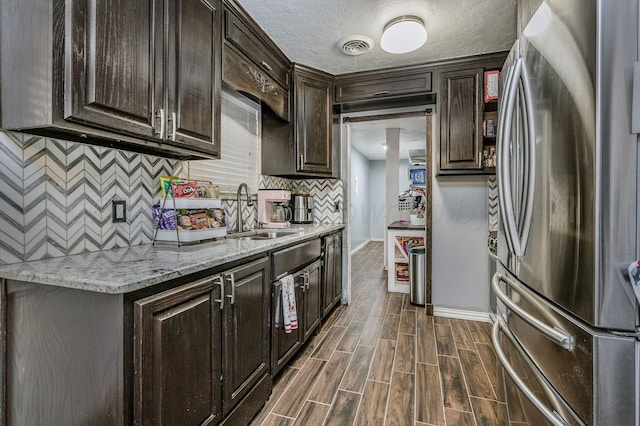 kitchen with tasteful backsplash, a sink, dark brown cabinetry, baseboards, and freestanding refrigerator
