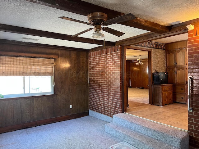 415 Mesquite Ave, Amarillo, TX 79108 - unfurnished room with a textured ceiling, a ceiling fan, beam ceiling, wood walls, and brick wall