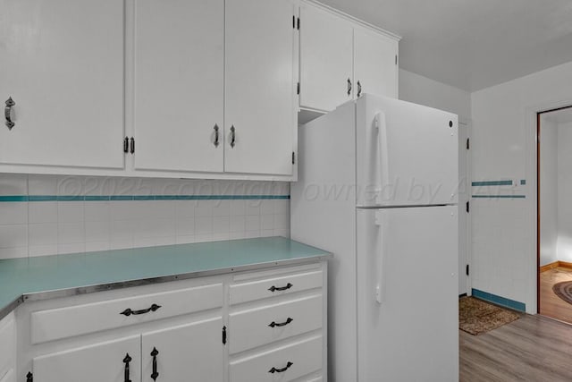 kitchen with light countertops, wood finished floors, freestanding refrigerator, and white cabinetry