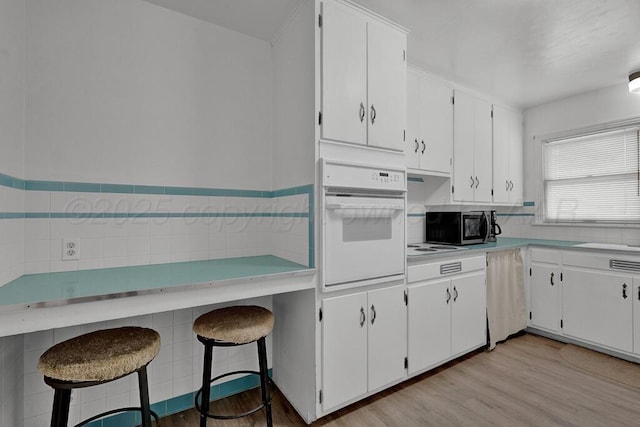 kitchen featuring white oven, stainless steel microwave, light countertops, light wood-style floors, and white cabinets