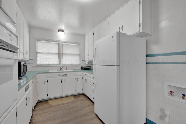 kitchen with a sink, white cabinets, light countertops, freestanding refrigerator, and light wood finished floors