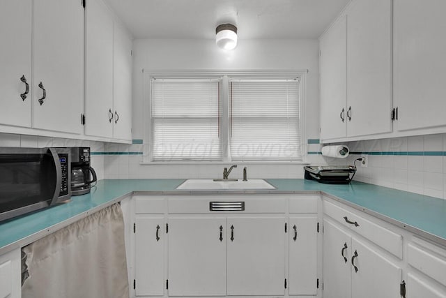 kitchen featuring stainless steel microwave, a sink, white cabinets, and decorative backsplash