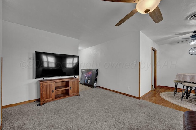 living room featuring baseboards, a ceiling fan, visible vents, and light colored carpet