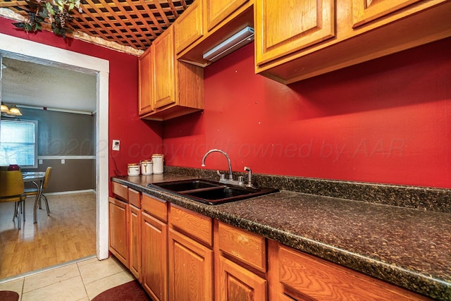 kitchen featuring dark countertops, light tile patterned flooring, brown cabinetry, and a sink