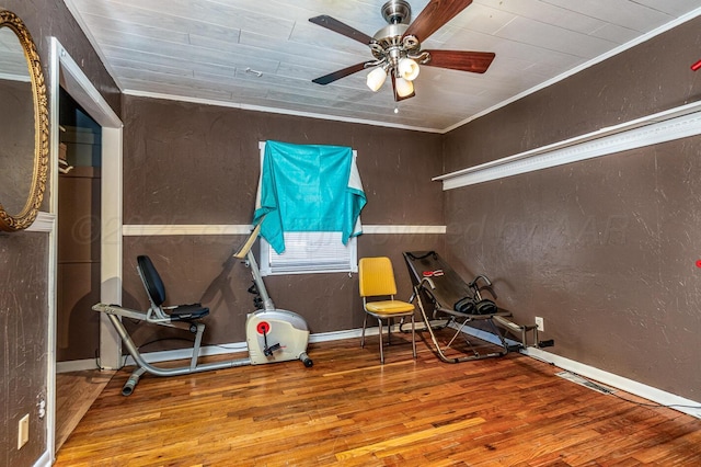 exercise area featuring wood finished floors, baseboards, ceiling fan, ornamental molding, and a textured wall