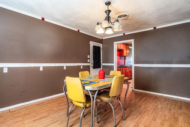 dining room featuring a notable chandelier, light wood-style floors, visible vents, and a textured ceiling