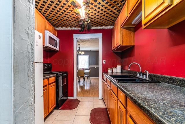 kitchen featuring white microwave, light tile patterned floors, brown cabinetry, black / electric stove, and a sink