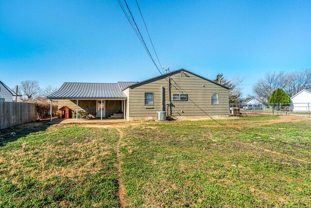 back of property with central AC unit, a yard, a fenced backyard, and metal roof