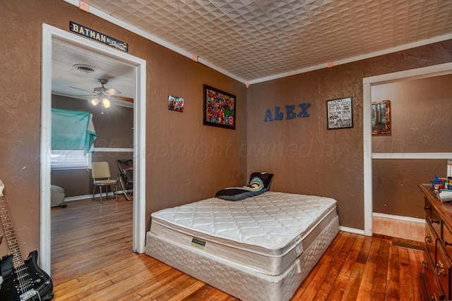 bedroom with visible vents, hardwood / wood-style floors, crown molding, baseboards, and a textured wall