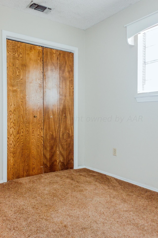 unfurnished bedroom with a textured ceiling, carpet flooring, and a closet