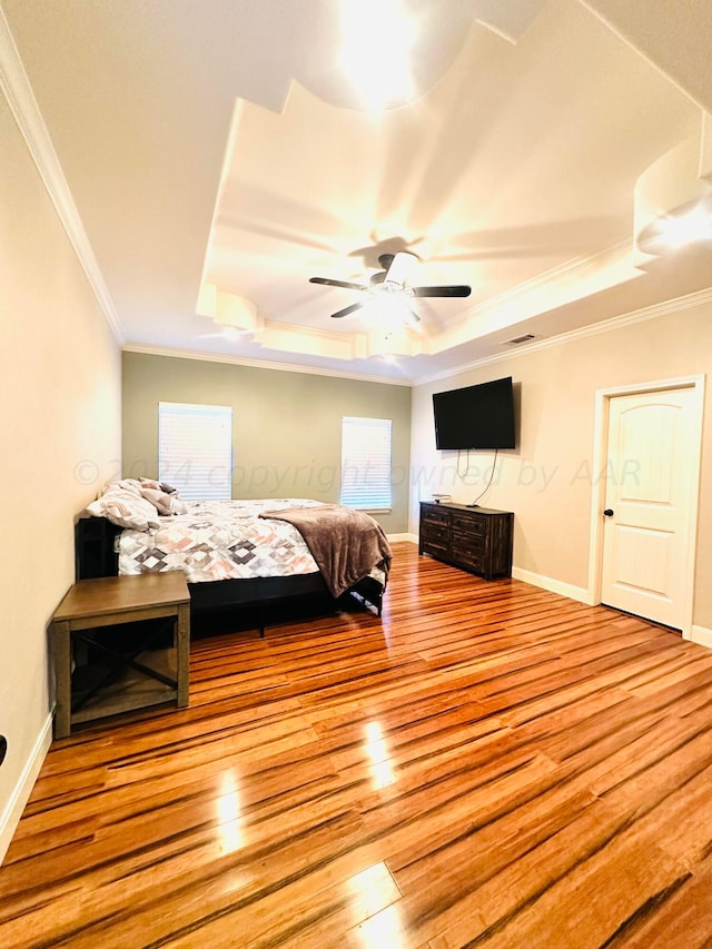 bedroom with ceiling fan, light hardwood / wood-style floors, a raised ceiling, and crown molding
