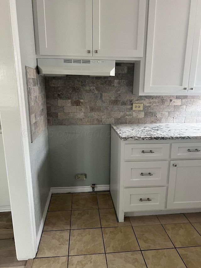 interior space featuring light tile patterned floors, light stone counters, white cabinetry, and under cabinet range hood