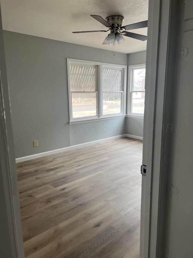 empty room with a textured ceiling, ceiling fan, wood finished floors, and baseboards