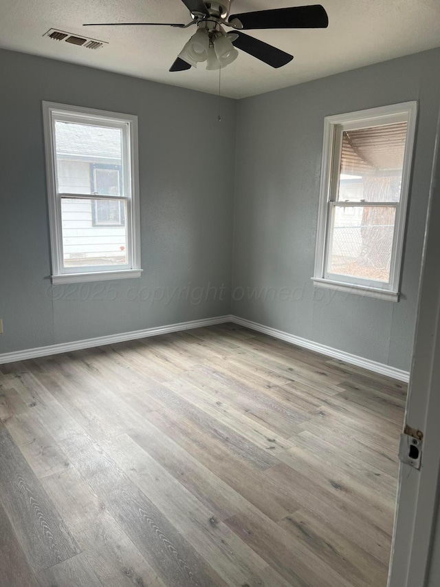 unfurnished room featuring baseboards, visible vents, wood finished floors, and a ceiling fan