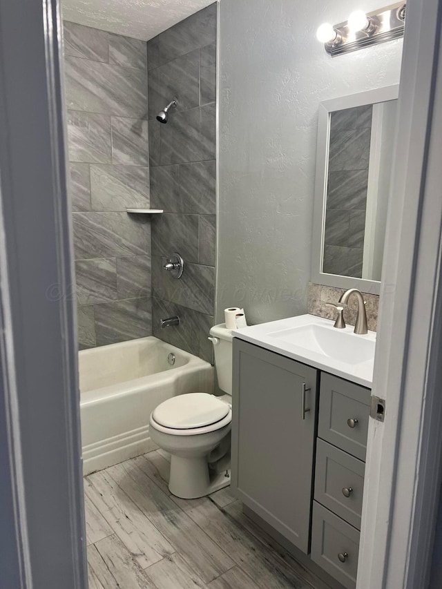 bathroom featuring vanity, toilet, a textured wall, wood finished floors, and  shower combination