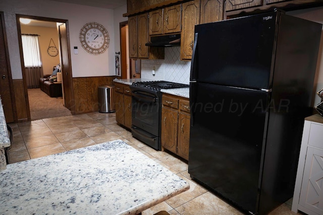 kitchen with tasteful backsplash, light tile patterned floors, wooden walls, and black appliances