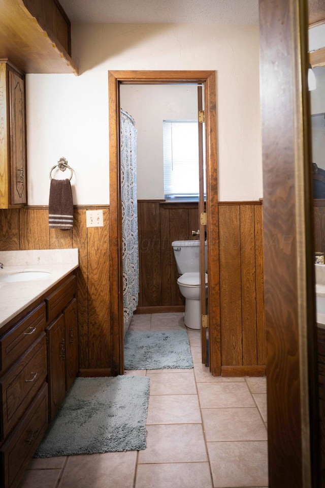 bathroom with toilet, tile patterned floors, vanity, and wooden walls