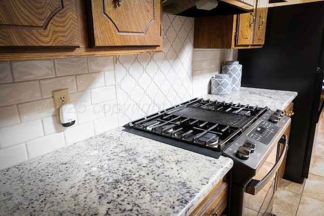 kitchen with tasteful backsplash, light tile patterned floors, light stone counters, and gas stove
