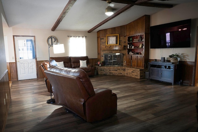 living room with dark wood-type flooring, wooden walls, lofted ceiling with beams, and a brick fireplace