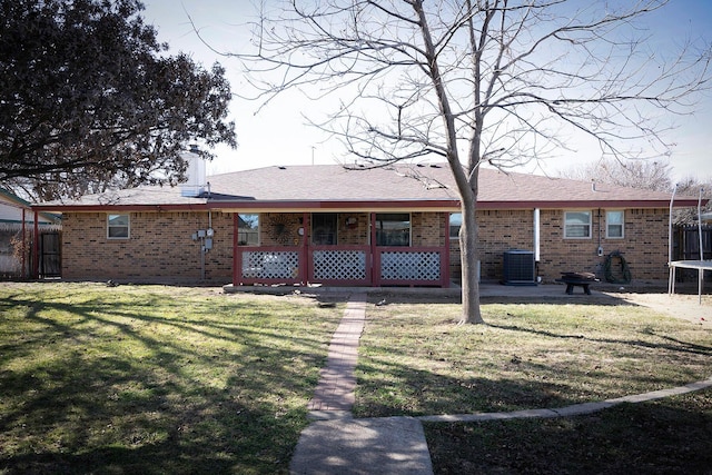 rear view of property featuring a trampoline, a yard, and central AC