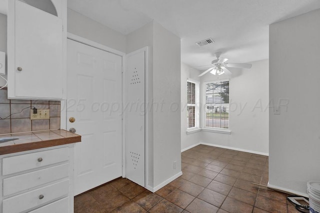 kitchen with tile countertops, white cabinetry, backsplash, ceiling fan, and baseboards