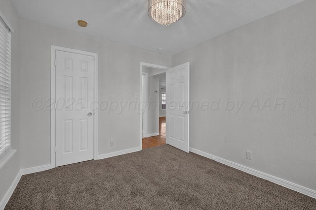 unfurnished bedroom with carpet, a chandelier, multiple windows, and baseboards