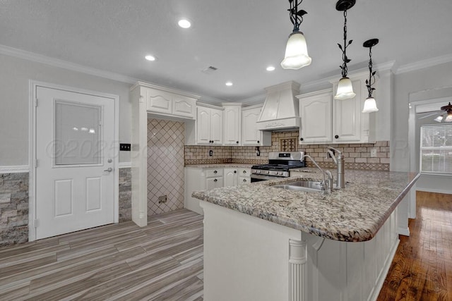 kitchen featuring custom exhaust hood, gas range, a sink, a peninsula, and light stone countertops