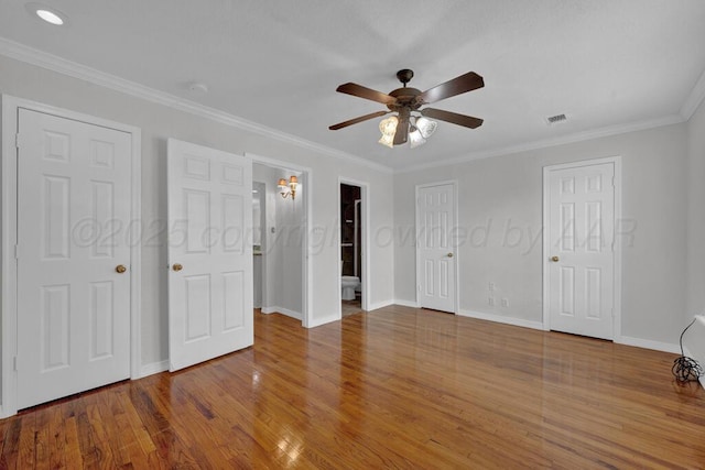 unfurnished bedroom with baseboards, wood finished floors, ornamental molding, multiple closets, and connected bathroom