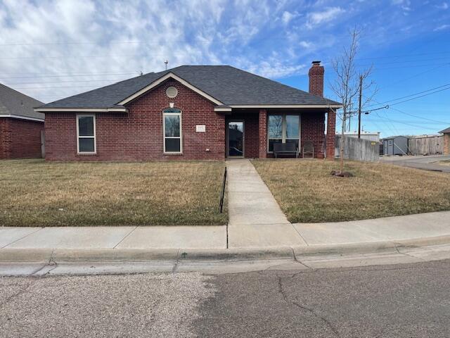 view of front of property with brick siding, a chimney, a front lawn, and roof with shingles