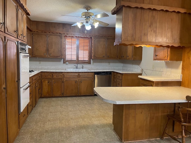 kitchen with dishwasher, sink, white oven, a kitchen breakfast bar, and kitchen peninsula