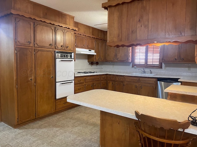 kitchen with sink, multiple ovens, stainless steel dishwasher, a textured ceiling, and kitchen peninsula