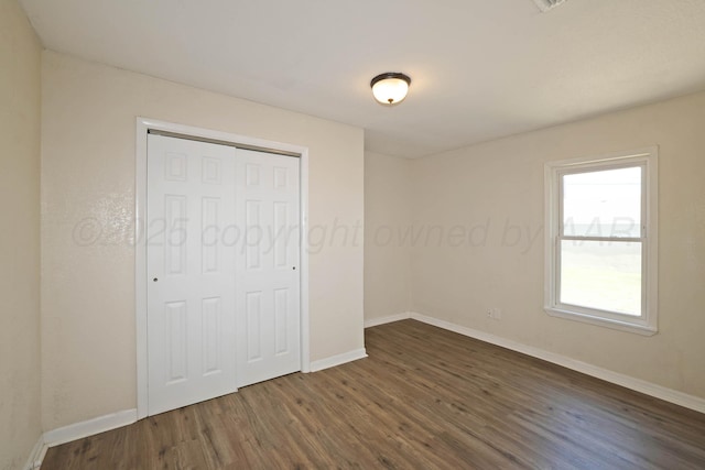 unfurnished bedroom with dark wood-style flooring, baseboards, and a closet
