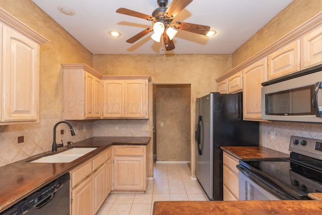 kitchen featuring light brown cabinets, light tile patterned floors, appliances with stainless steel finishes, dark countertops, and a sink