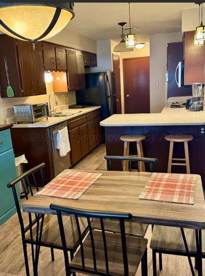 kitchen with a kitchen breakfast bar, hanging light fixtures, light wood-type flooring, dark brown cabinets, and stainless steel appliances