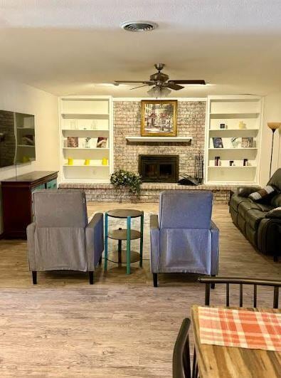 living room with ceiling fan, built in features, light wood-type flooring, and a brick fireplace