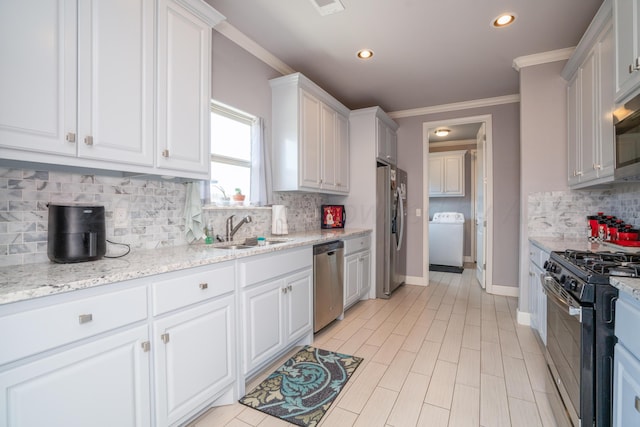 kitchen featuring decorative backsplash, appliances with stainless steel finishes, a sink, washer / dryer, and white cabinetry
