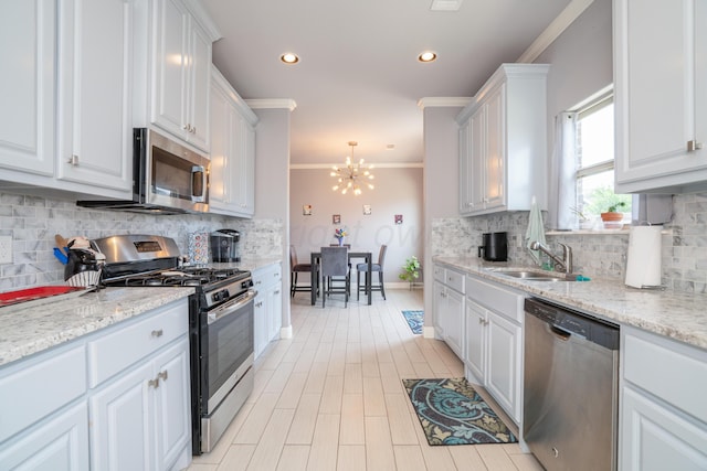 kitchen with white cabinets, a sink, a chandelier, stainless steel appliances, and ornamental molding