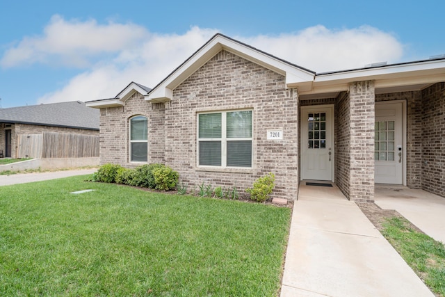 ranch-style home with brick siding, fence, and a front yard