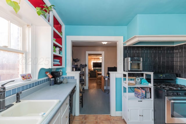 kitchen with stainless steel gas stove, a sink, light countertops, white cabinetry, and backsplash