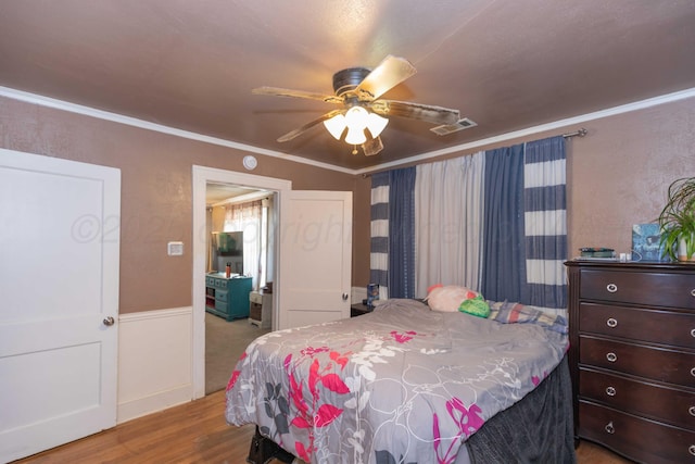 bedroom featuring ceiling fan, ornamental molding, wood finished floors, and visible vents