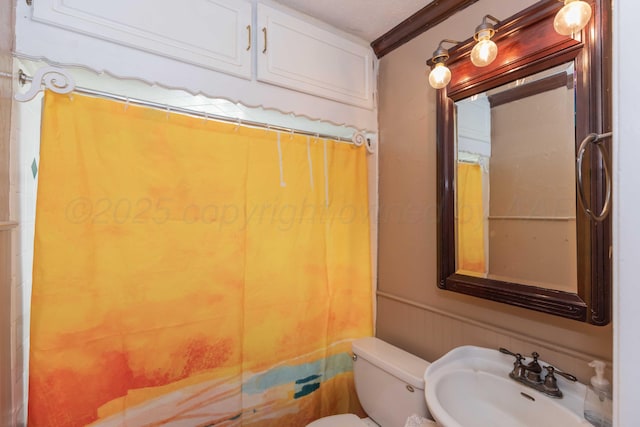 full bathroom with a wainscoted wall, a shower with shower curtain, toilet, ornamental molding, and a sink